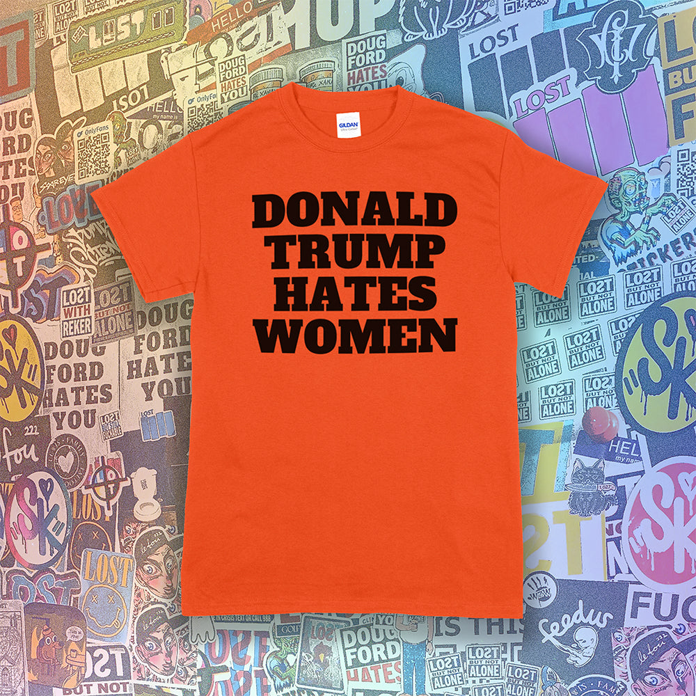 Donald Trump Hates Women t-shirt. Bold letters screen printed with black ink on an orange shirt. A huge amount of graffiti stickers in the background.