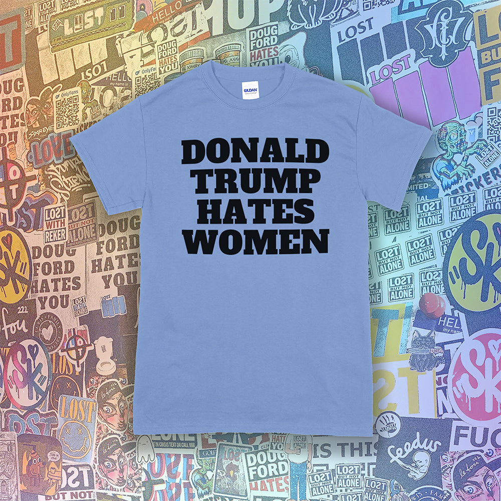 Donald Trump Hates Women t-shirt. Bold letters screen printed with black ink on a Carolina blue shirt. A huge amount of graffiti stickers in the background.