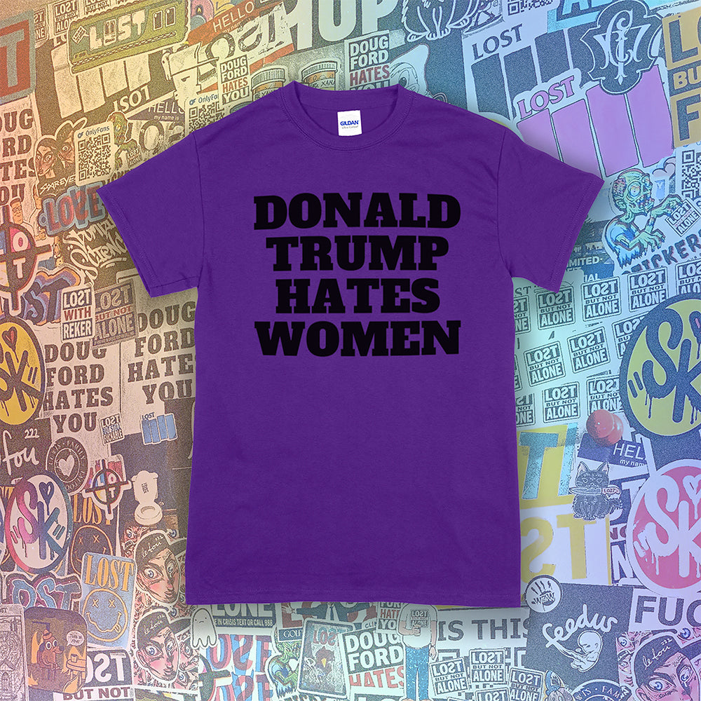 Donald Trump Hates Women t-shirt. Bold letters screen printed with black ink on a purple shirt. A huge amount of graffiti stickers in the background.