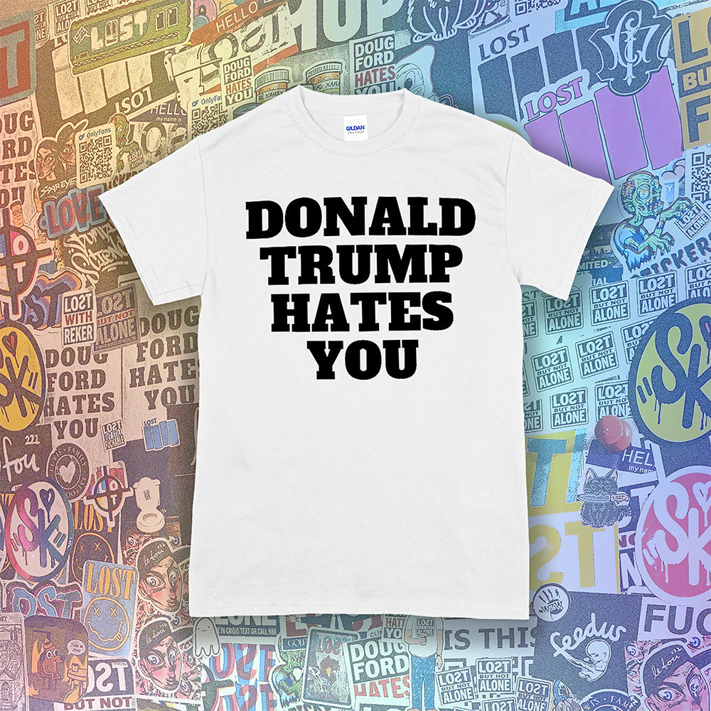 Donald Trump Hates You t-shirt. Bold letters screen printed with black ink on a white shirt. Assorted colorful graffiti stickers in the background.