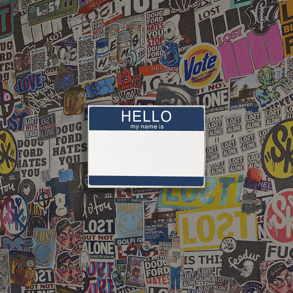 Hello my name is blank nametag sticker. A blue and white nametag sticker waiting to be tagged. The sticker is set against a wall of colorful graffiti stickers.