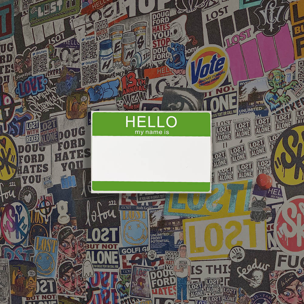 Hello my name is blank nametag sticker. A green and white nametag sticker waiting to be tagged. The sticker is set against a wall of colorful graffiti stickers.