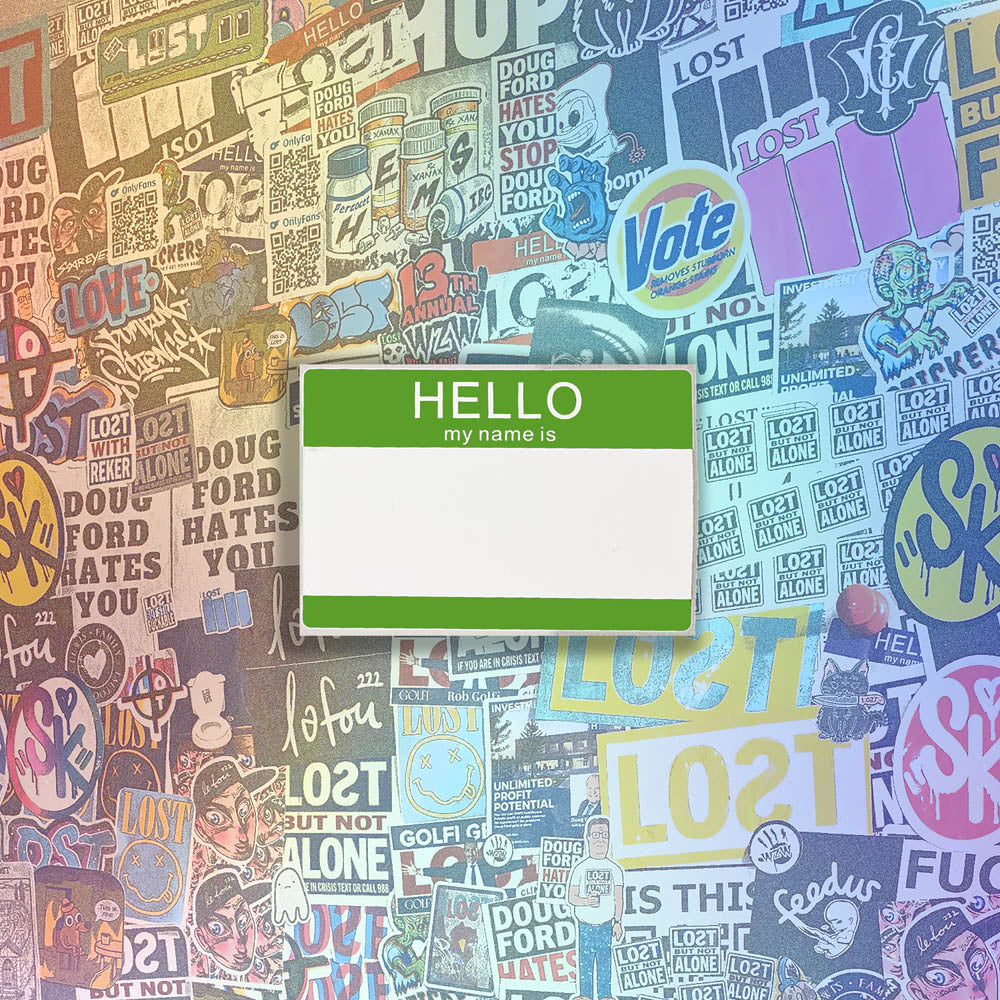 Hello my name is blank nametag sticker. A green and white nametag sticker waiting to be tagged. The sticker is set against a wall of colorful graffiti stickers.