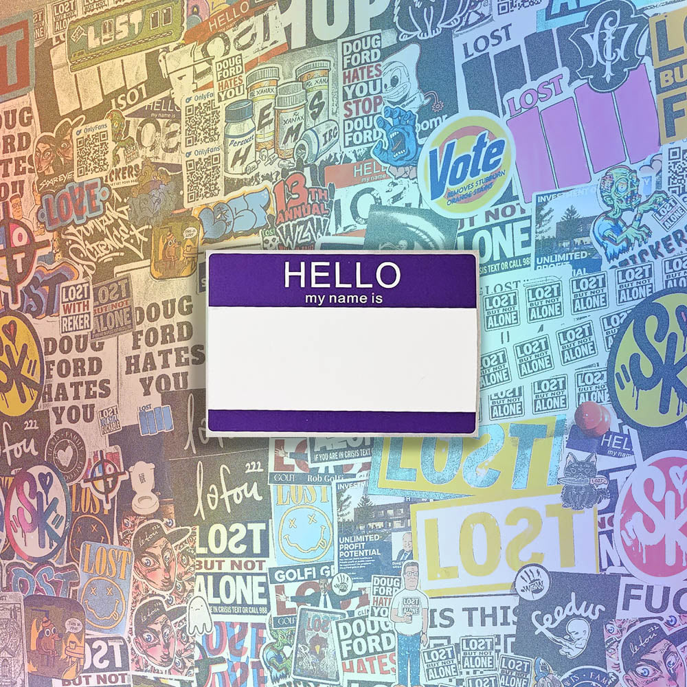 Hello my name is blank nametag sticker. A purple and white nametag sticker waiting to be tagged. The sticker is set against a wall of colorful graffiti stickers.