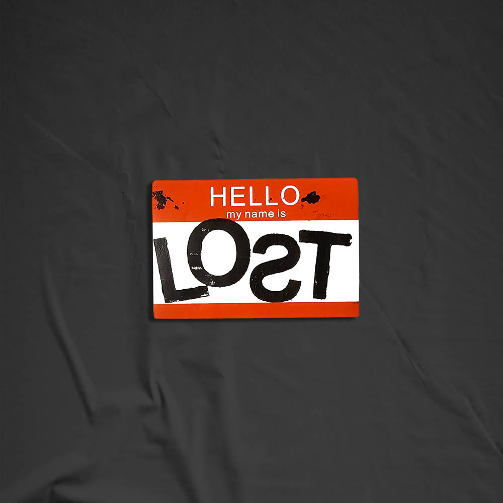 Hello my name is LOST sticker. A red and white nametag sticker stamped with the name LOST with a backwards S. The sticker is set against a black background.