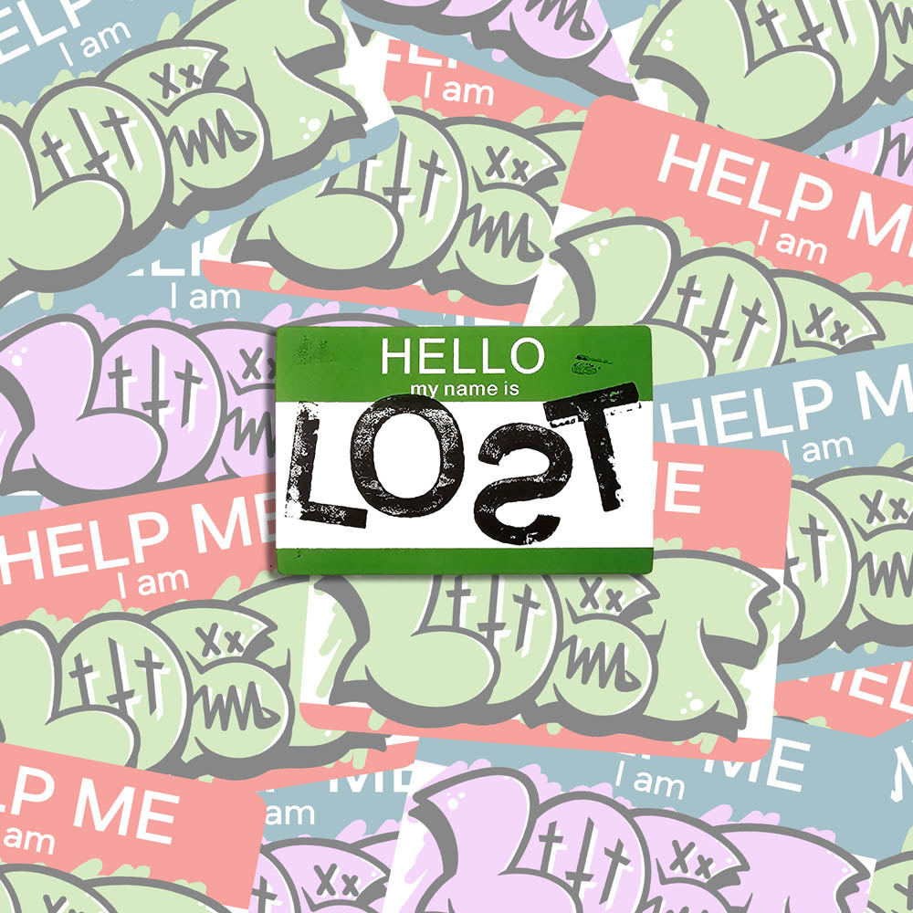 A hand stamped graffiti sticker by LOST. Black print of the word LOST on a rectangular green and white nametag sticker with rounded corners. The sticker is shown against a wall of colorful graffiti stickers.