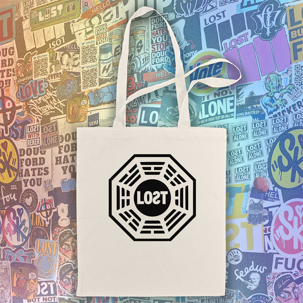 The bold and iconic octagon logo with the word LOST printed in bold black ink and displayed on a large natural canvas tote bag. A wall of colorful graffiti stickers featuring artists from around the world creates a vibrant background for the tote bag on display.  