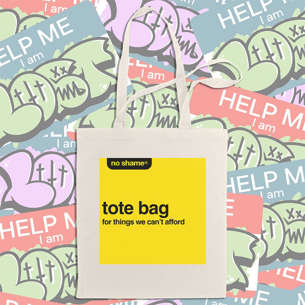 The no shame tote bag: for things we can't afford. Those words are screen  printed in bold black ink inside a no name yellow box on a large, natural canvas tote bag. A wall of colorful graffiti stickers creates a vibrant background for the tote bag on display.  