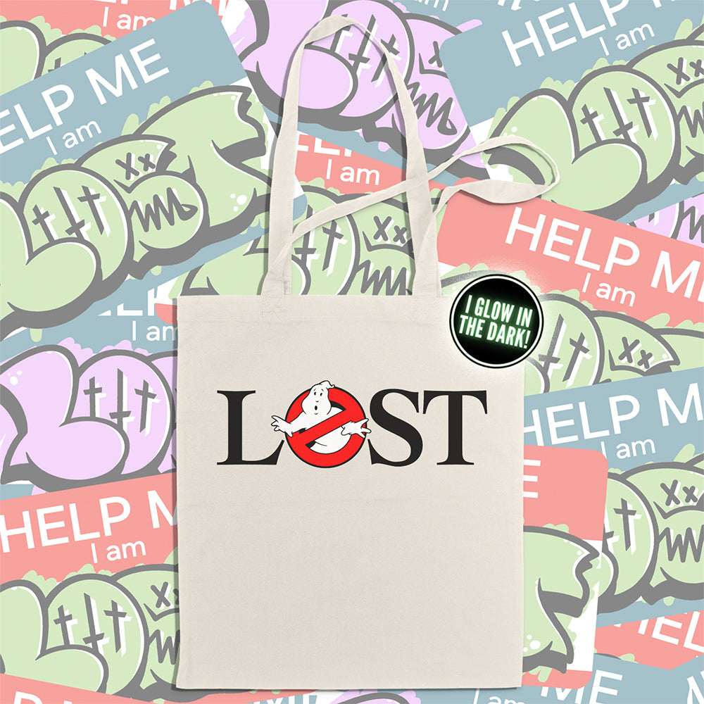 The LOSTBUSTERS tote bag features a surprised looking  ghost trapped in the O of the word LOST and vaguely resembling the original Ghostbusters logo. The crisp image is screen printed on a natural canvas tote bag. A wall of colorful graffiti stickers creates a vibrant background for the tote bag on display.