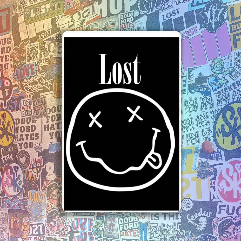 The In Bloom sticker by LOST. Black and white smiley face design with  LOST written above it. A wall of colorful graffiti stickers provides a unique background for the sticker.