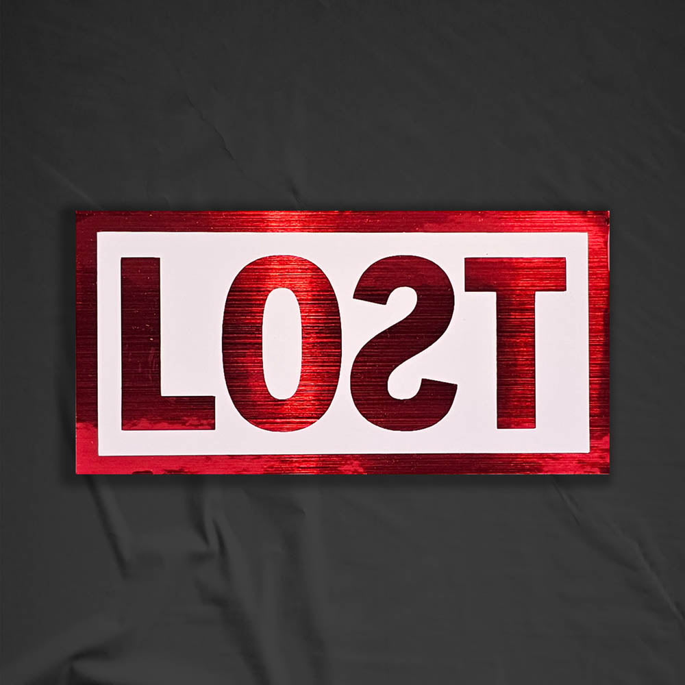 The original graffiti sticker by LOST. A simple two color cut design featuring the word LOST written with a backwards S in metallic red and contained within a matte white rectangle. The sticker is set against a contrasting black background.