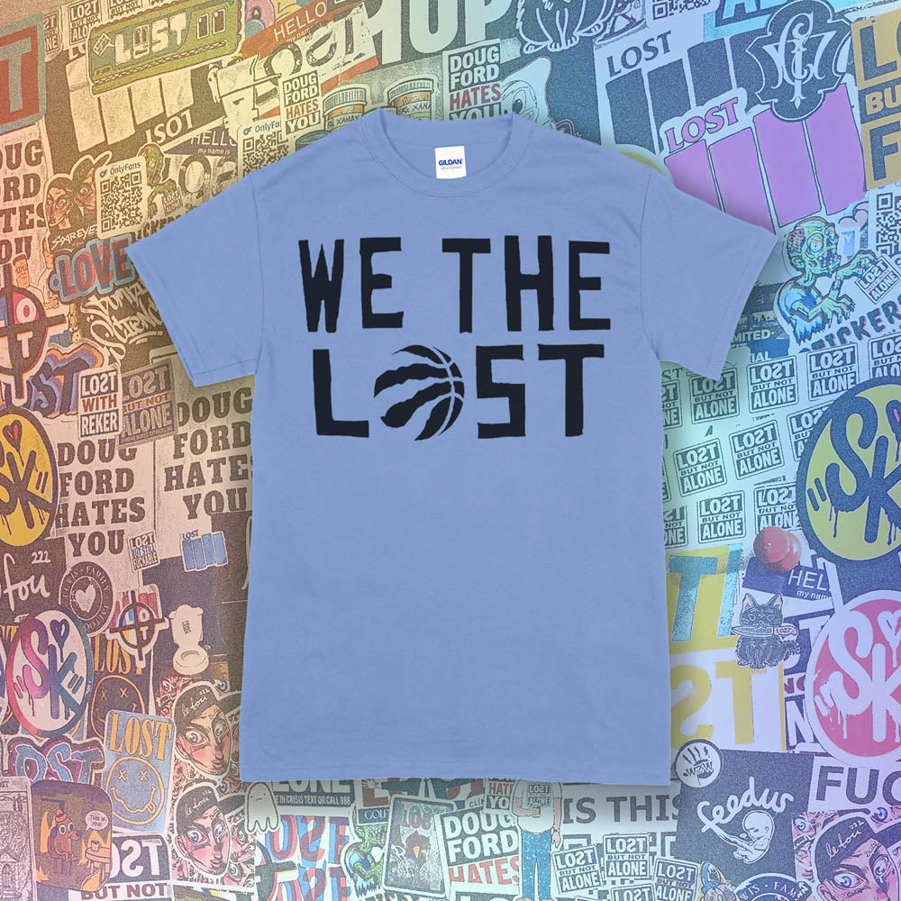 We The Lost t-shirt. Bold black lettering and raptor claw design screen printed on a light blue shirt. A wall of colorful graffiti stickers make up the background.