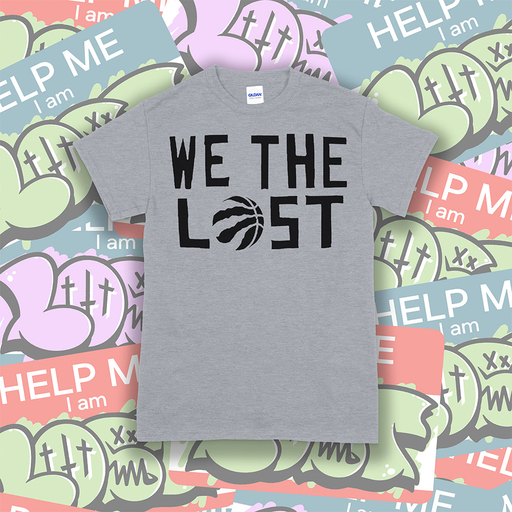 We The Lost t-shirt. Bold black lettering screen printed on a gray shirt. Assorted colorful graffiti stickers make up the background.